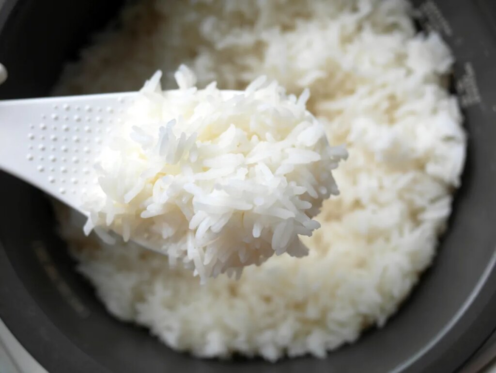 top view close-up of cooked jasmine white rice in the white ladle with background of electric rice cooker