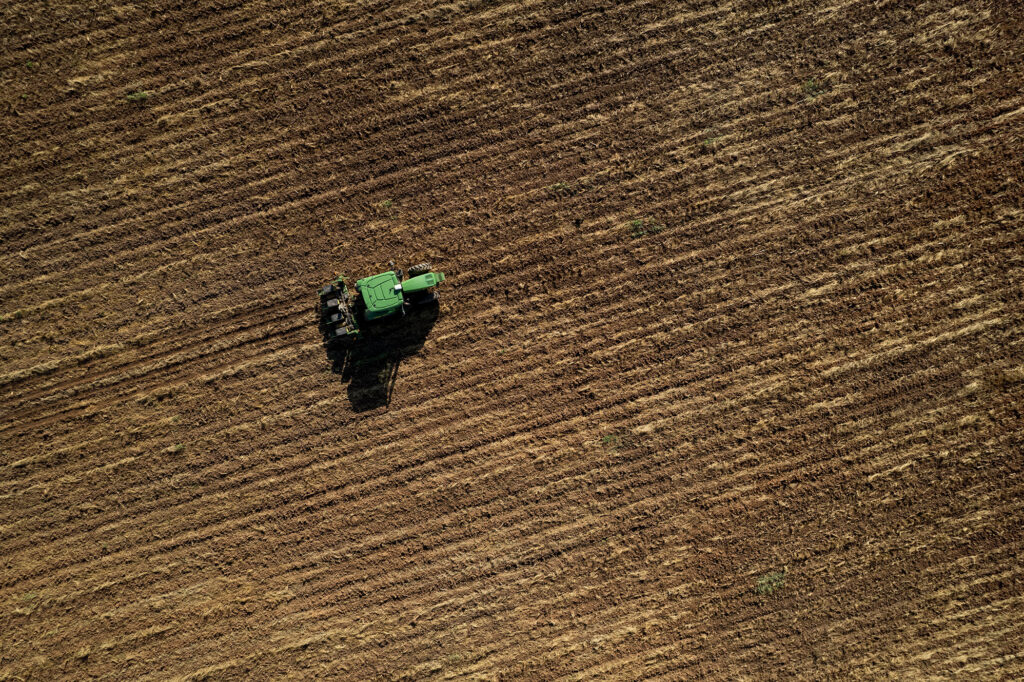 A green tractor is going down a red-brown dirt field.